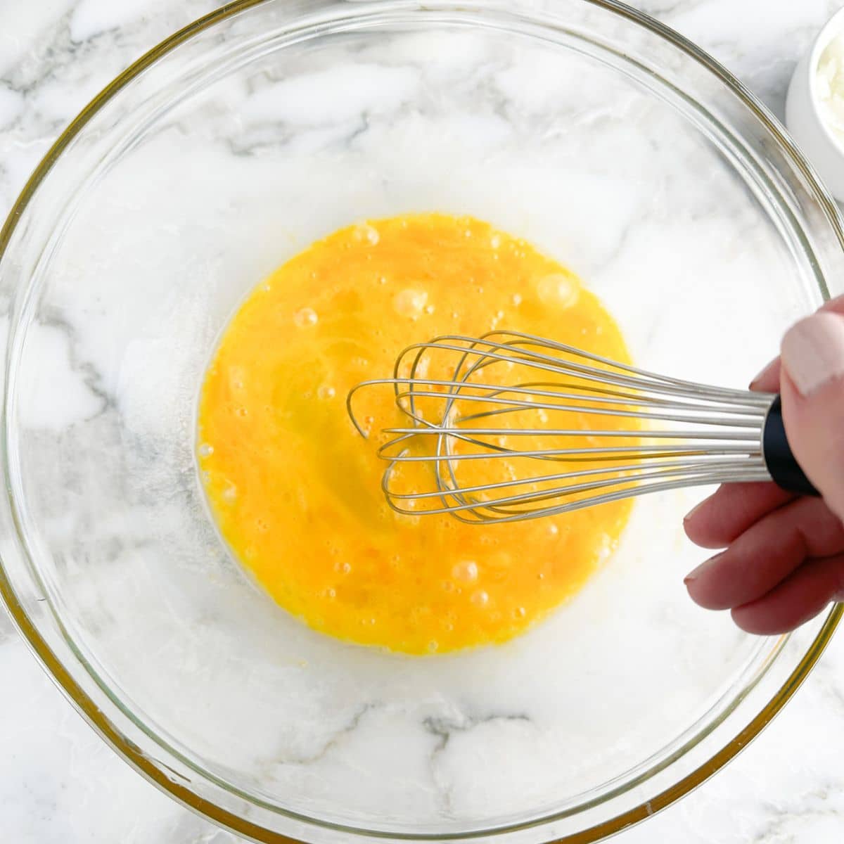 Bowl with beaten eggs and a whisk.