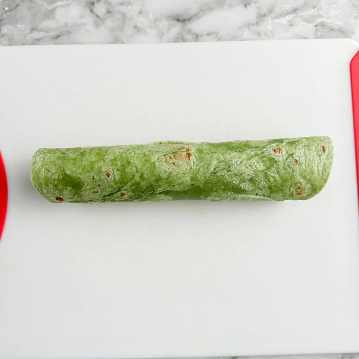 Green tortilla rolled up on a cutting board.