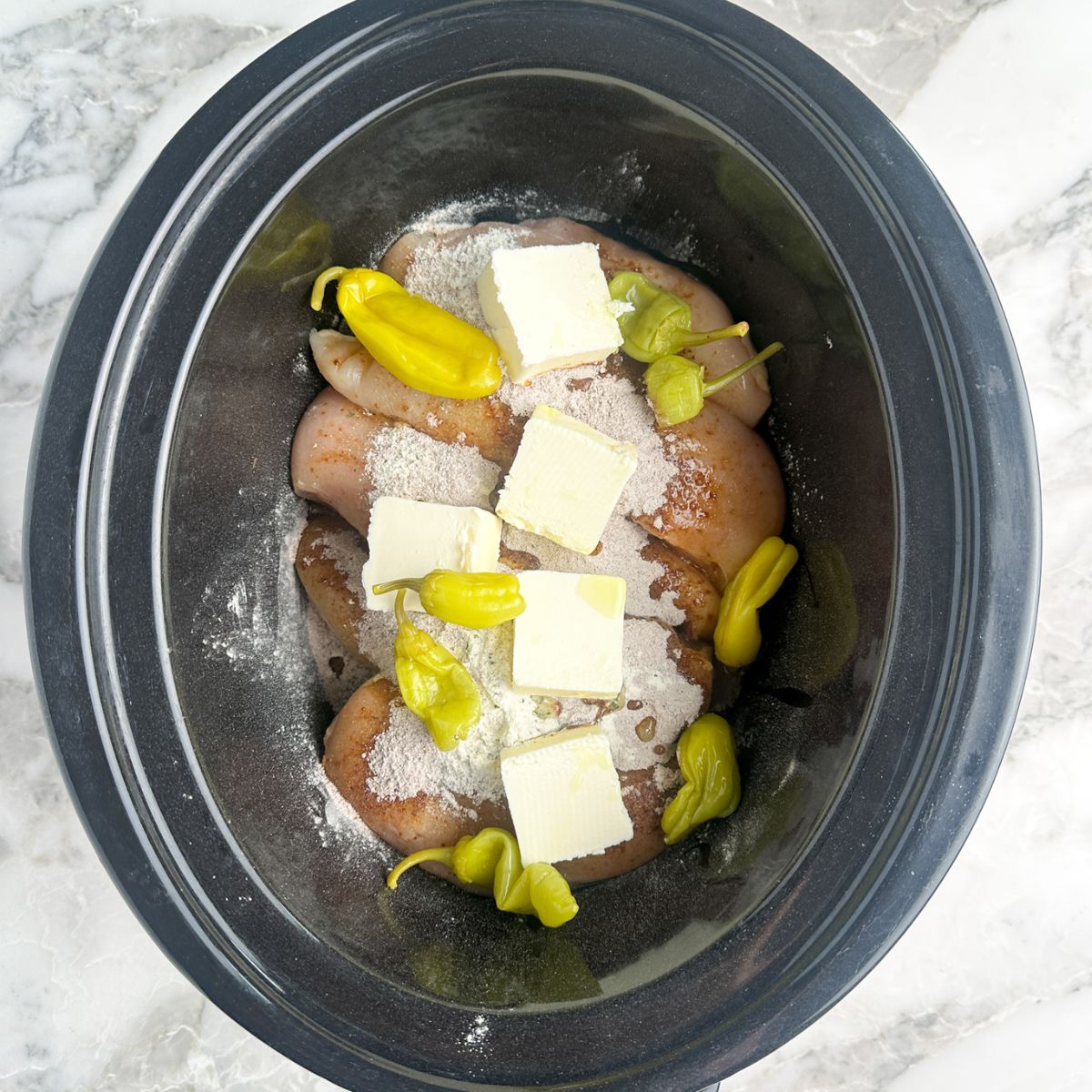 Slow cooker with chicken, seasonings, peppers, and butter. 