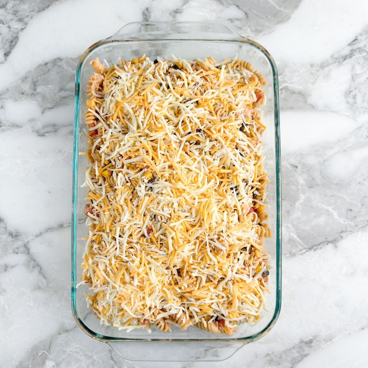 Casserole dish with chicken and pasta, topped with shredded cheese.