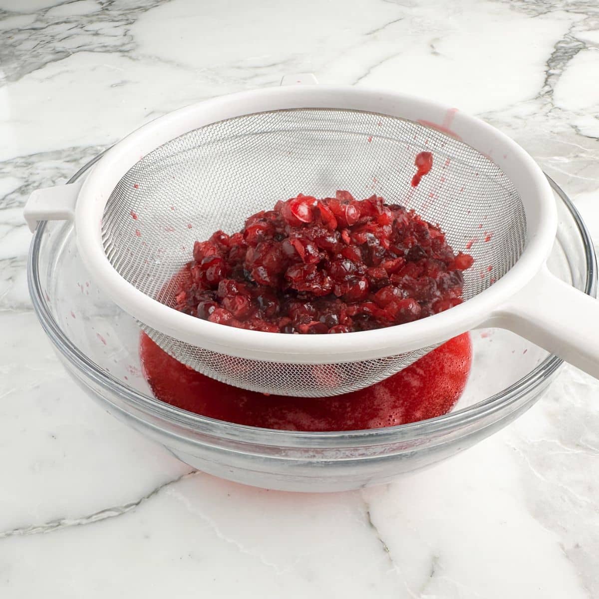 Strainer with cranberries and cranberry juice.