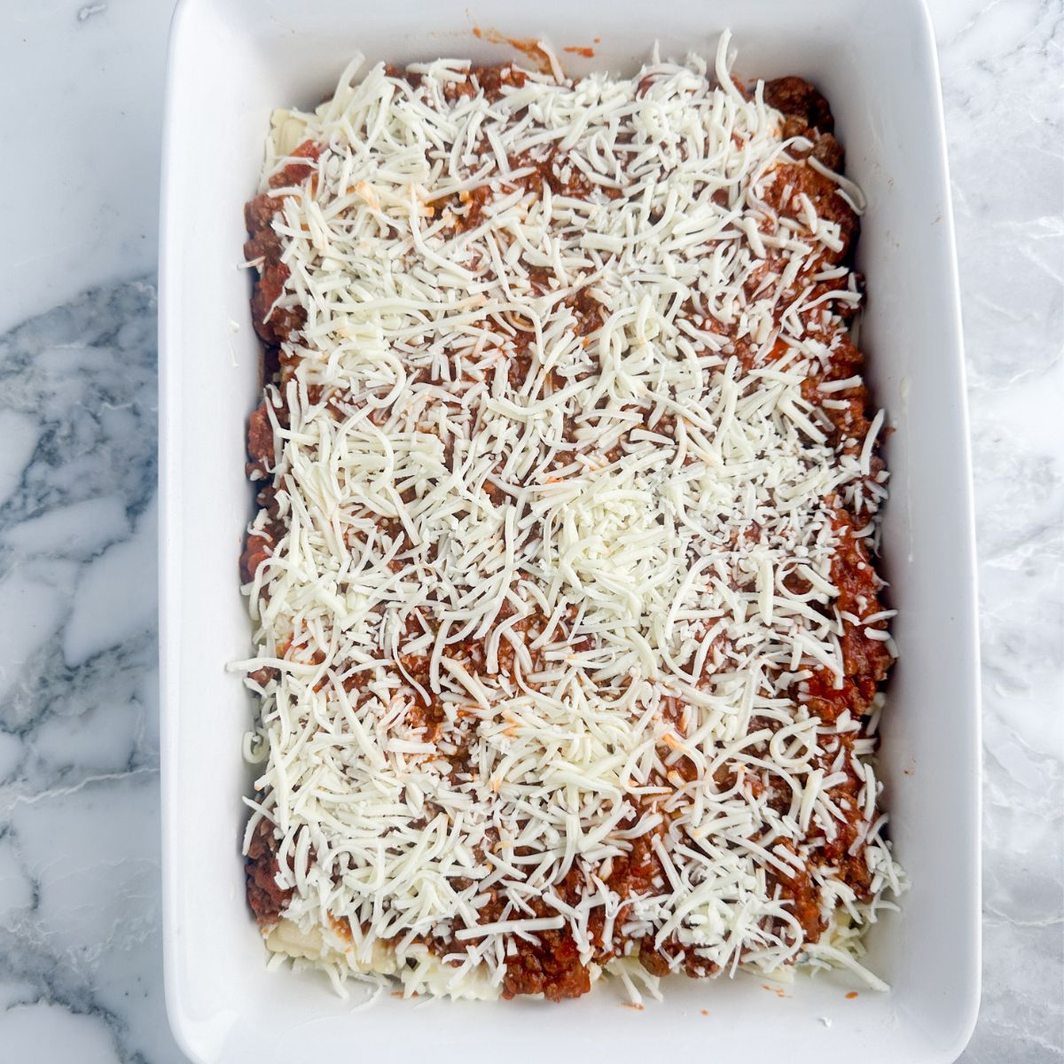 Baking dish with meat sauce and shredded cheese. 