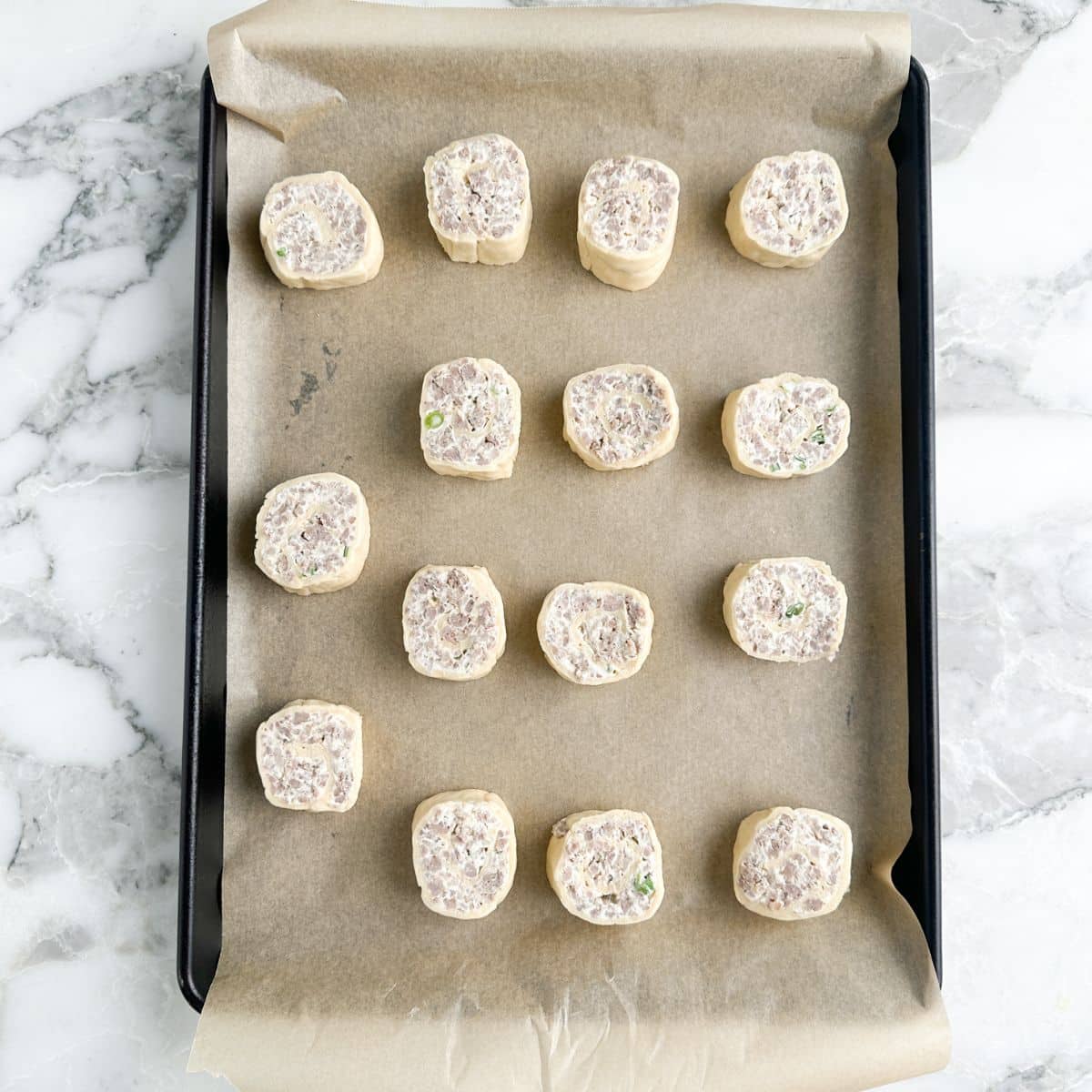 Unbaked sausage rolls on a baking sheet.