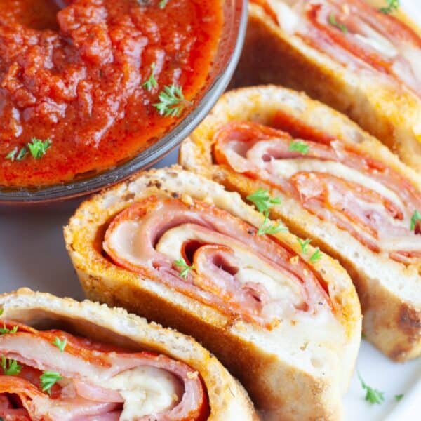 Sliced stromboli on a plate with a bowl of marinara sauce.