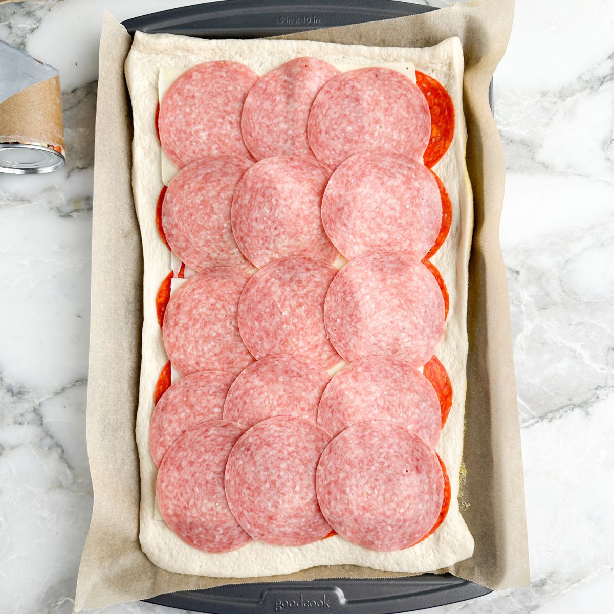 Pizza dough with pepperoni, cheese, and sliced salami. 