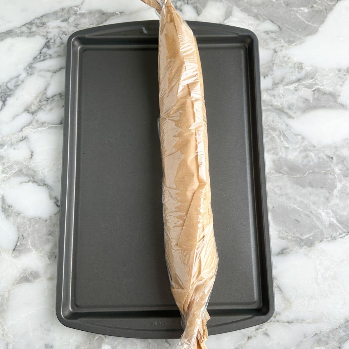 Sausage roll in plastic wrap on a baking sheet.