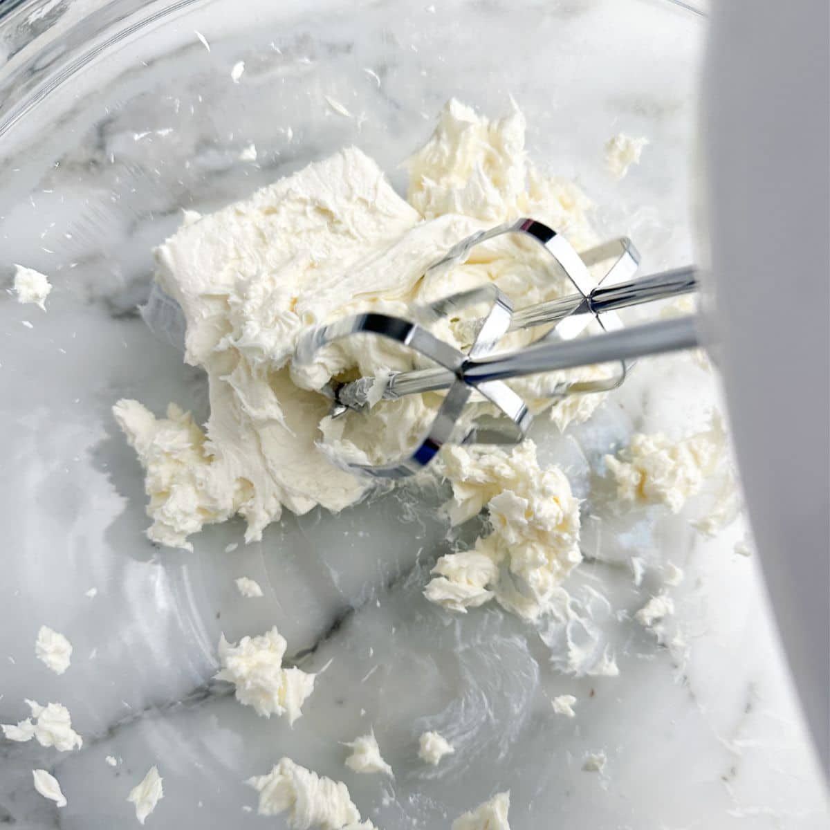 Glass bowl with beaten cream cheese and a mixer. 