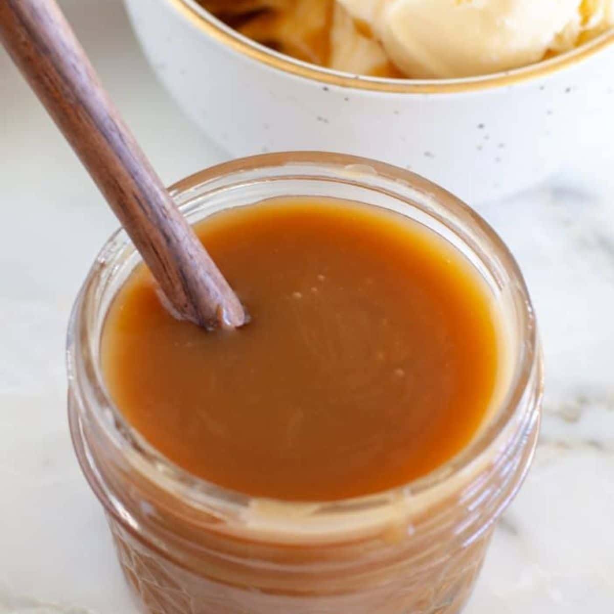 Jar of butterscotch sauce with a wooden spoon.