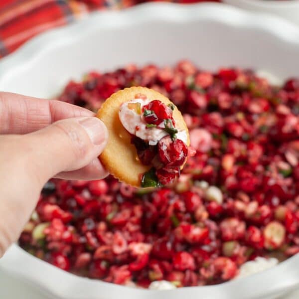 Hand holding a cracker with cranberry jalapeno dip.