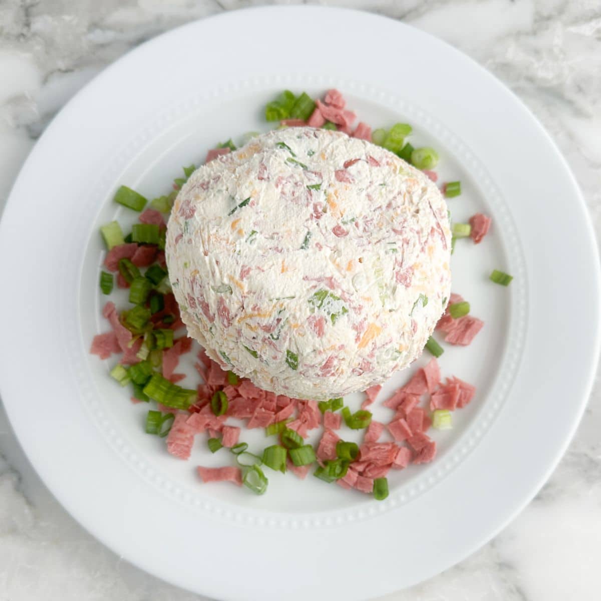 Cheese ball on a plate with chipped beef and green onions. 