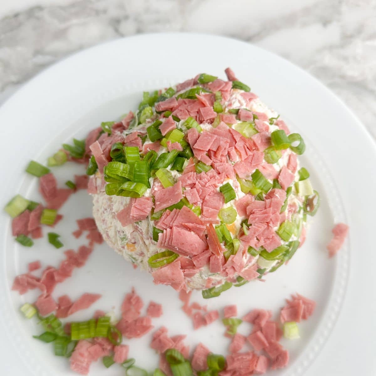 Cheese ball with chipped beef and green onions on a plate.