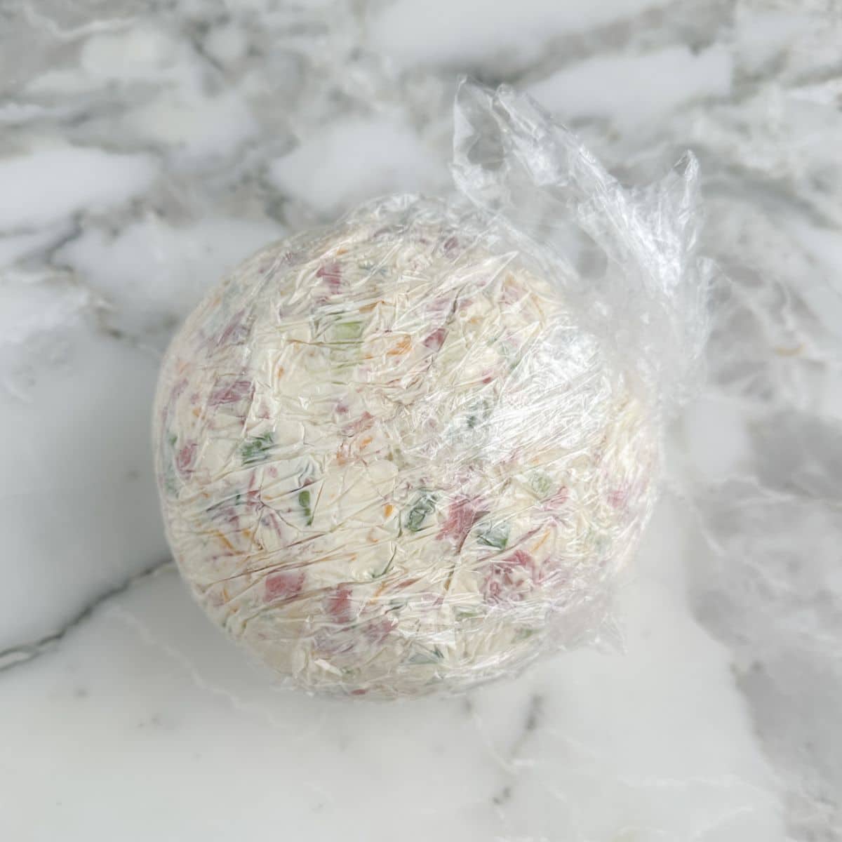 Cheese ball wrapped in plastic wrap.