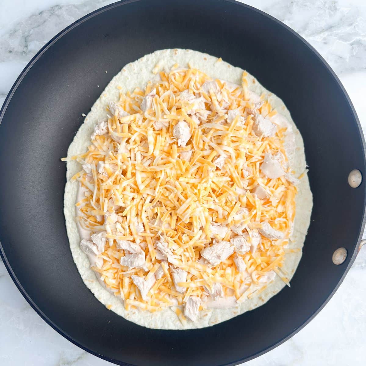 Tortilla in a pan topped with cheese and chicken.