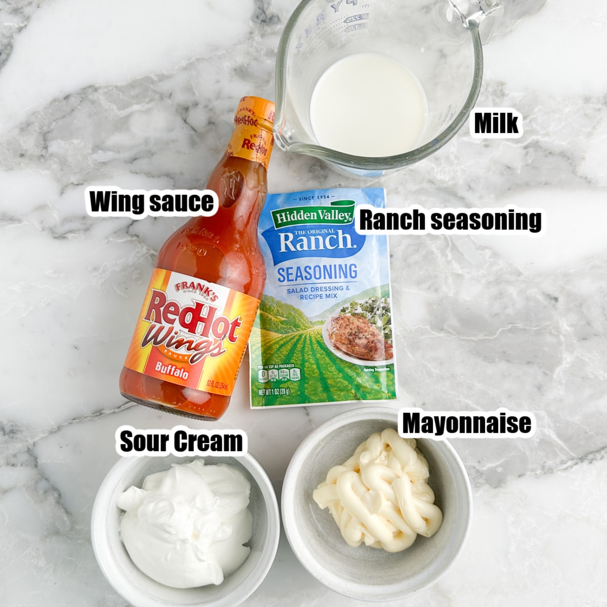 Bottle of wing sauce, ranch seasonings, bowls of sour cream, mayonnaise, and milk. 