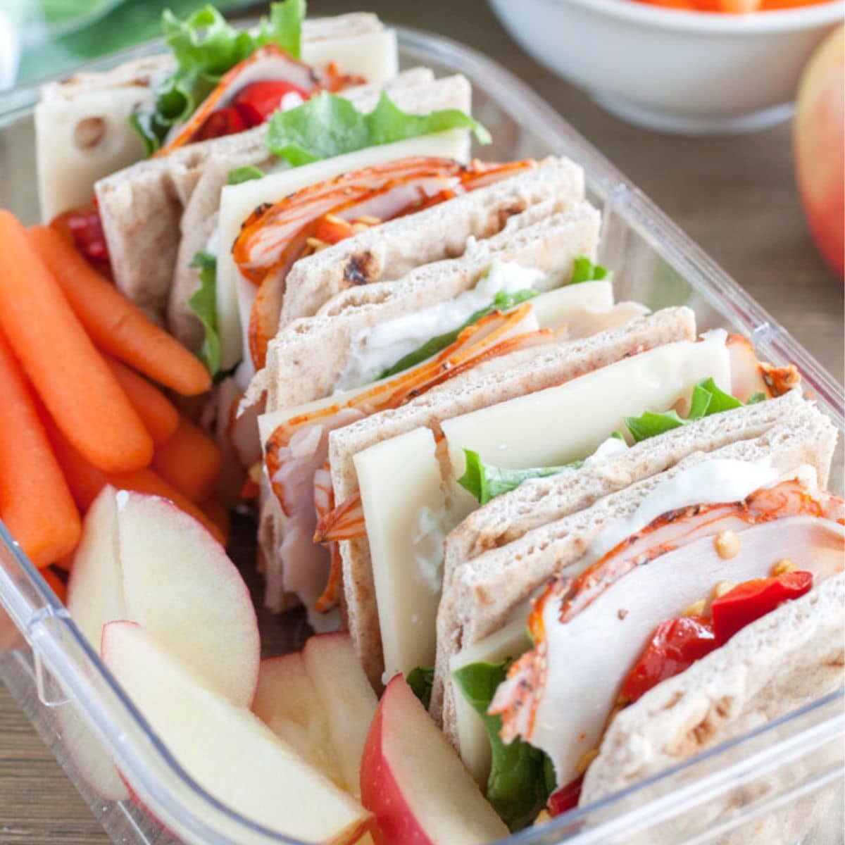 Box with a sandwich, apples, and carrots.