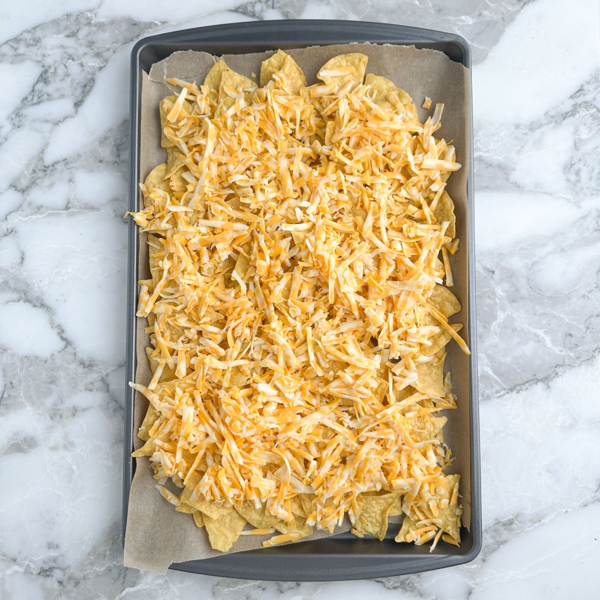 Baking sheet with tortilla chips and shredded cheese. 