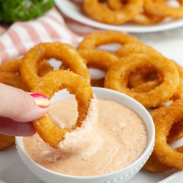 Onion ring dipping into bloomin onion sauce.