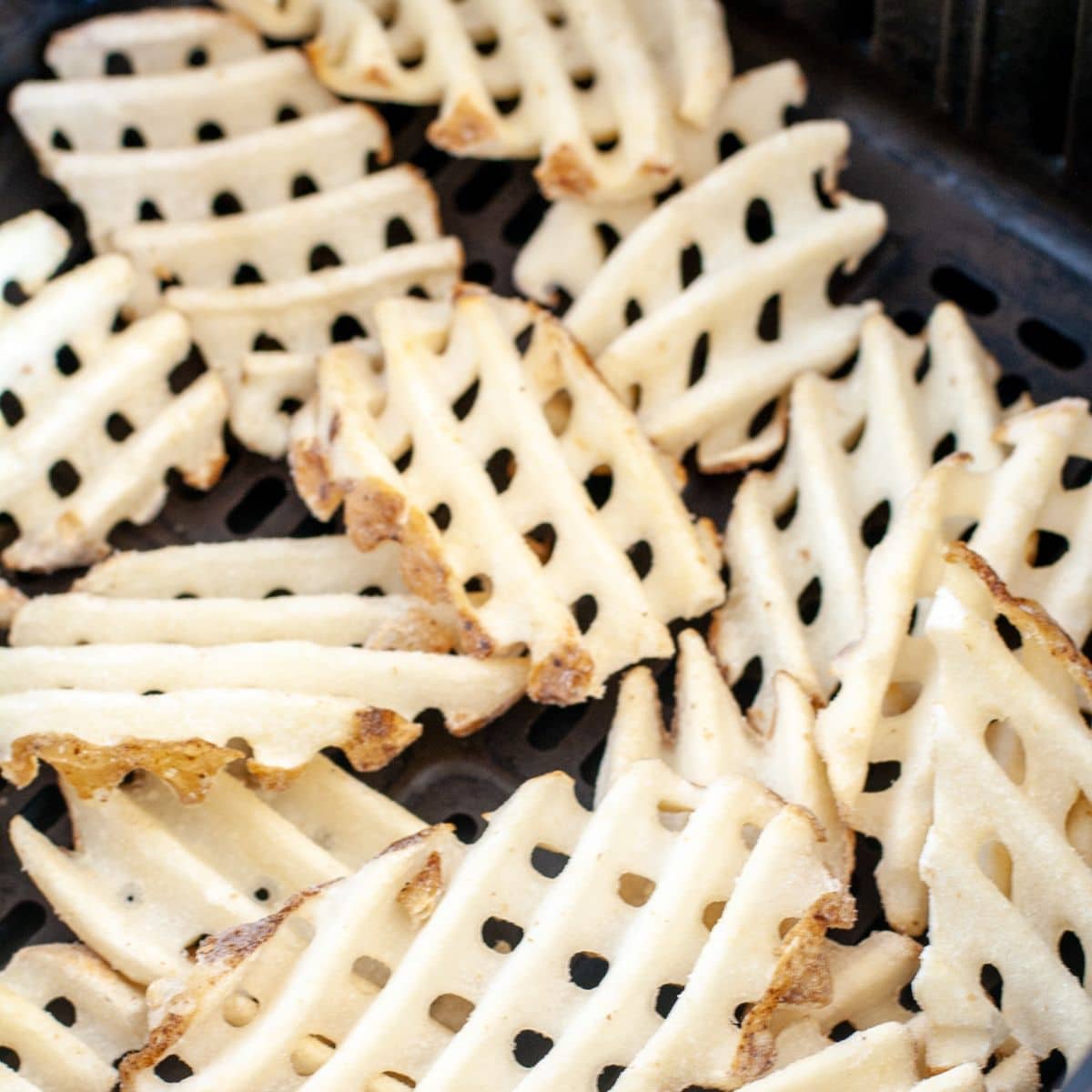 Frozen waffle fries in an air fryer basket.