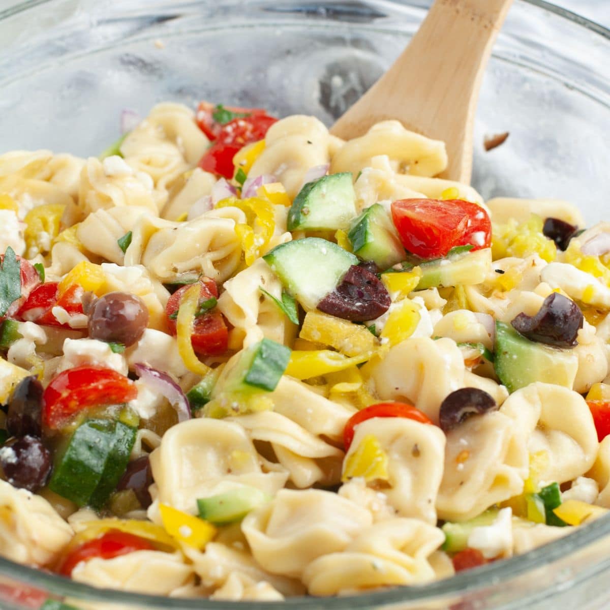 Bowl of tortellini pasta salad with a wooden spoon.