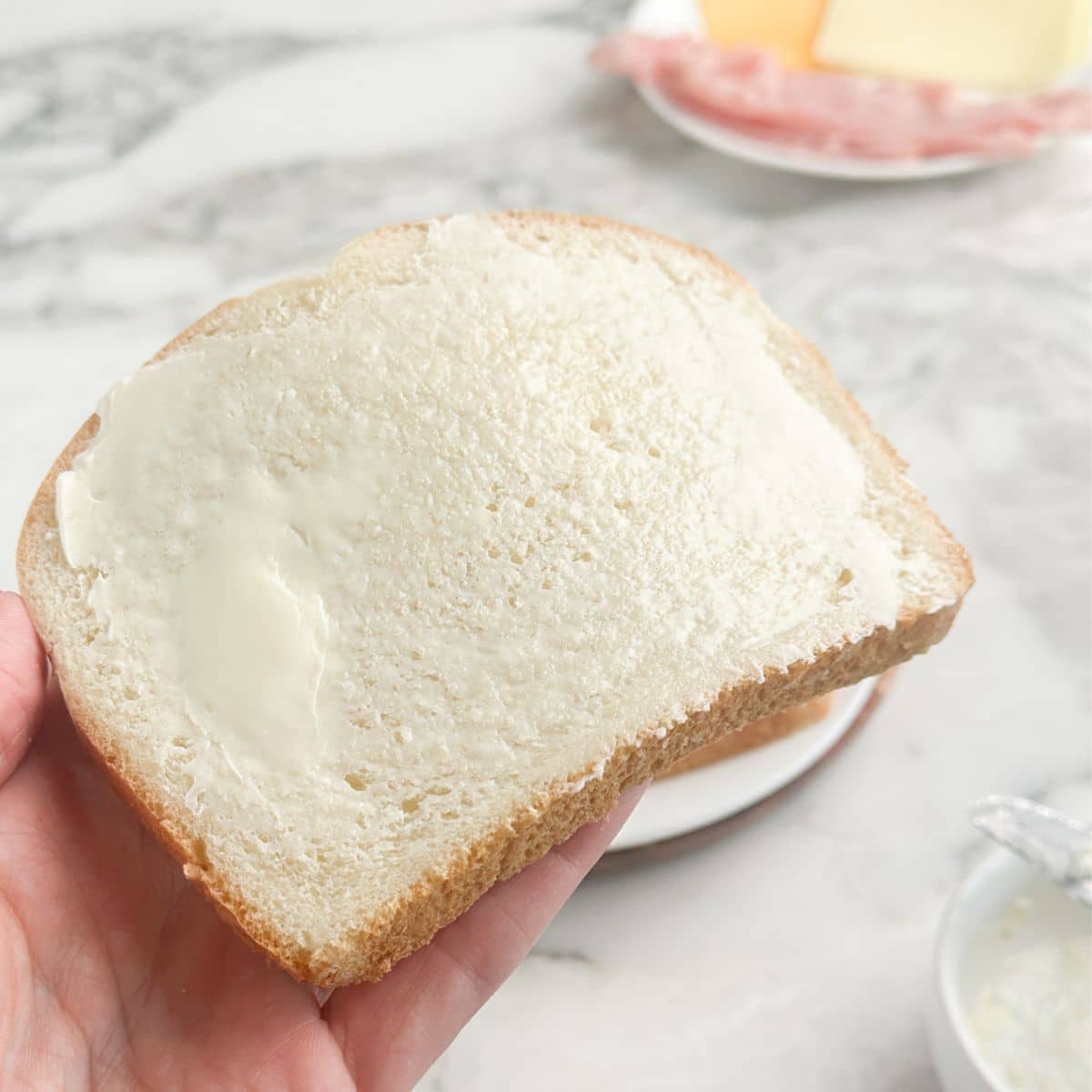 Hand holding a slice of bread with butter.