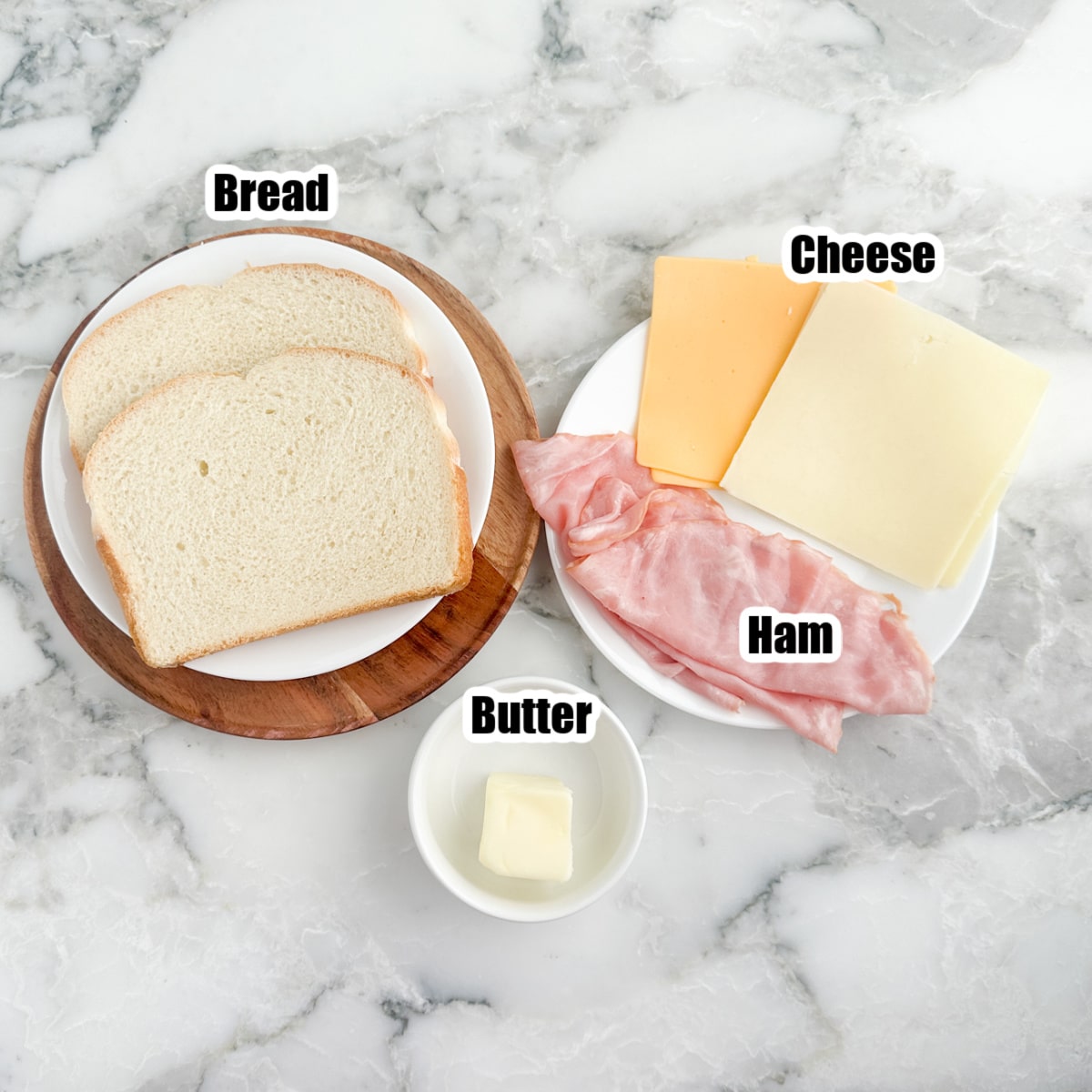 Plate of bread, sliced cheese, deli ham, and butter. 