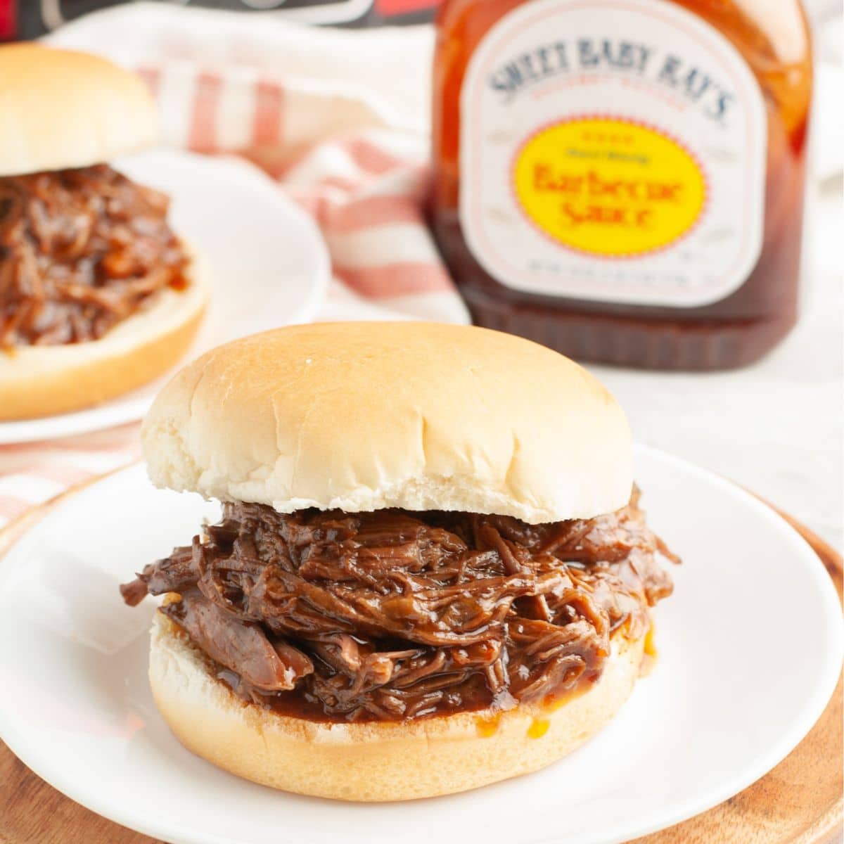 BBQ beef sandwich on a plate with a bottle of BBQ sauce. 