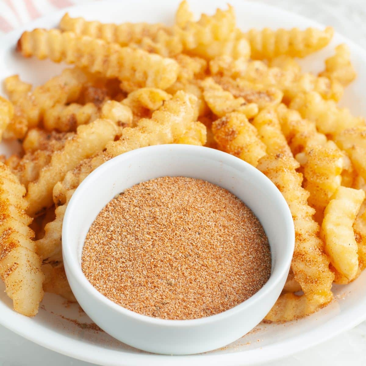 Bowl of seasoning with crinkled fries. 