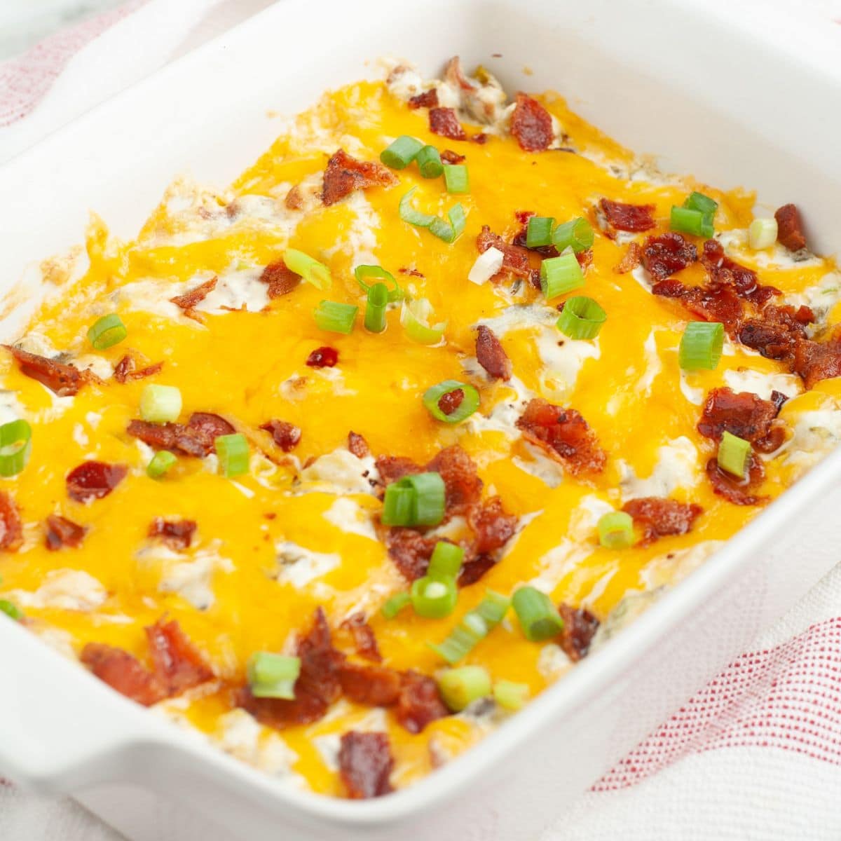 Baking dish with cooked jalapeno popper dip topped with melted cheese, bacon, and green onion. 