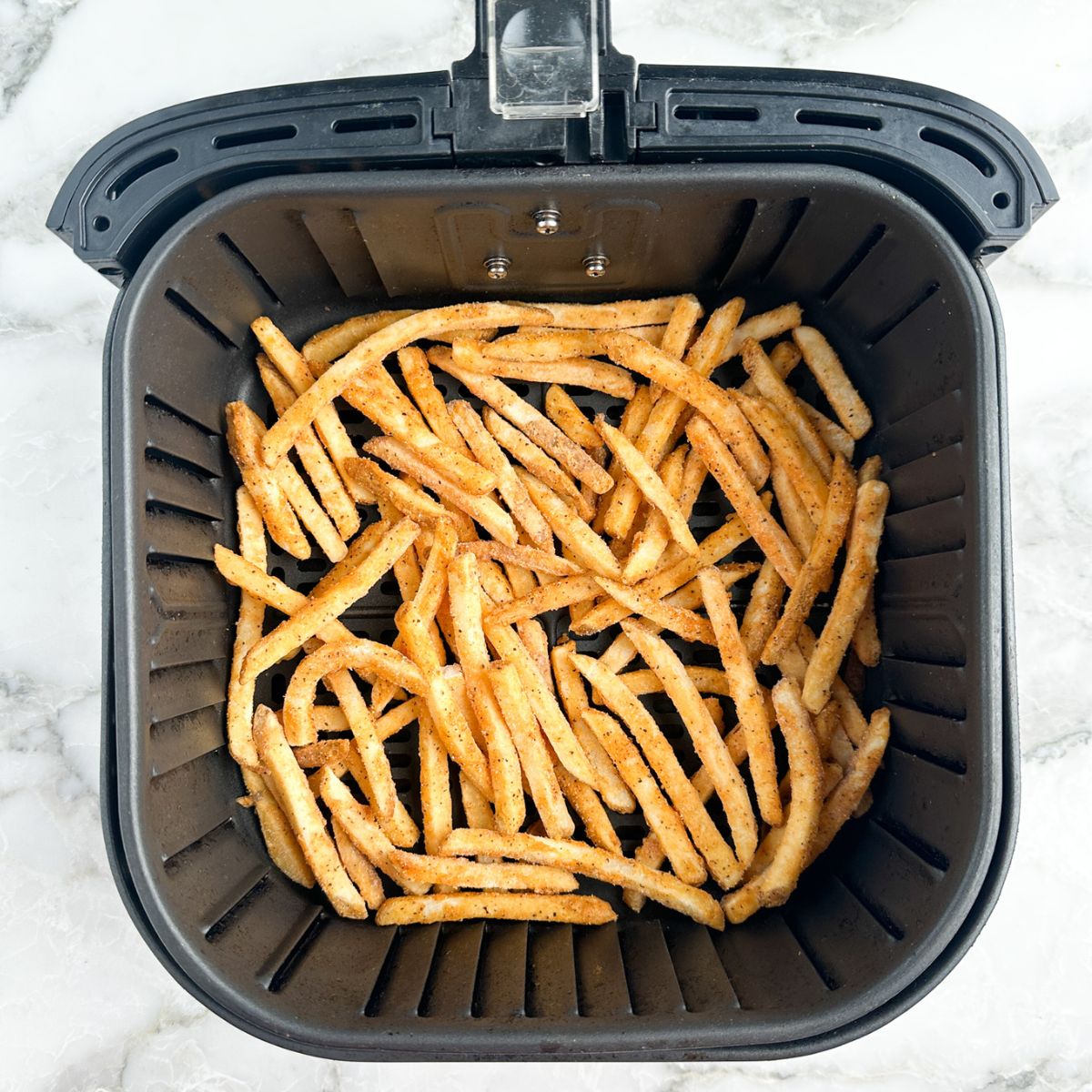 Frozen french fries in an air fryer basket. 