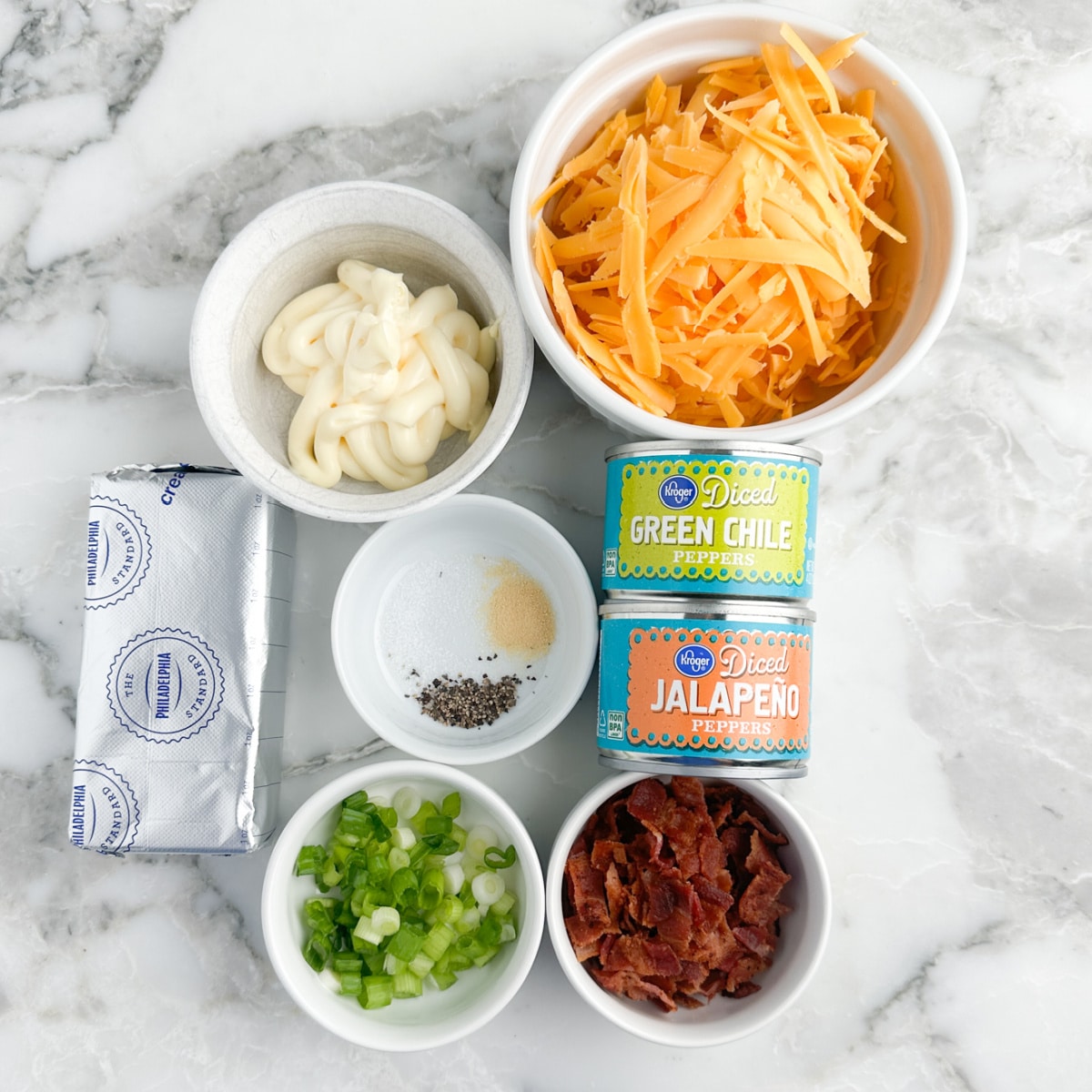 Cream cheese, bowl of mayonnaise, shredded cheese, diced green onions, crumbled bacon, cans of green chile peppers, and diced jalapenos. 