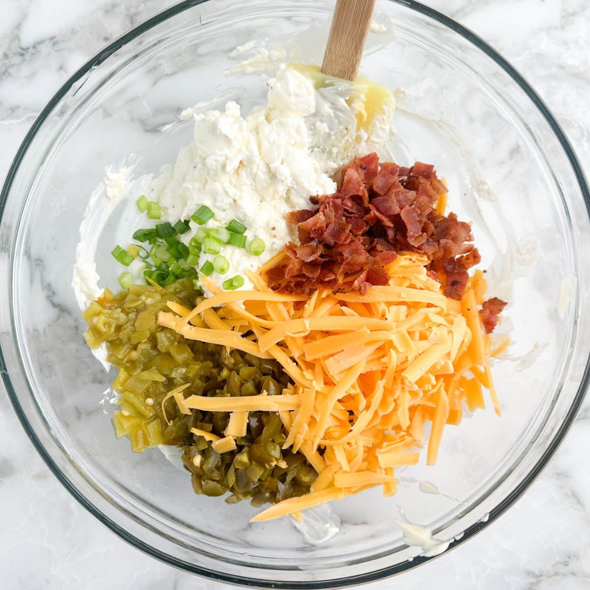 Large bowl with cream cheese, shredded cheese, crumbled bacon, and diced green onion. 