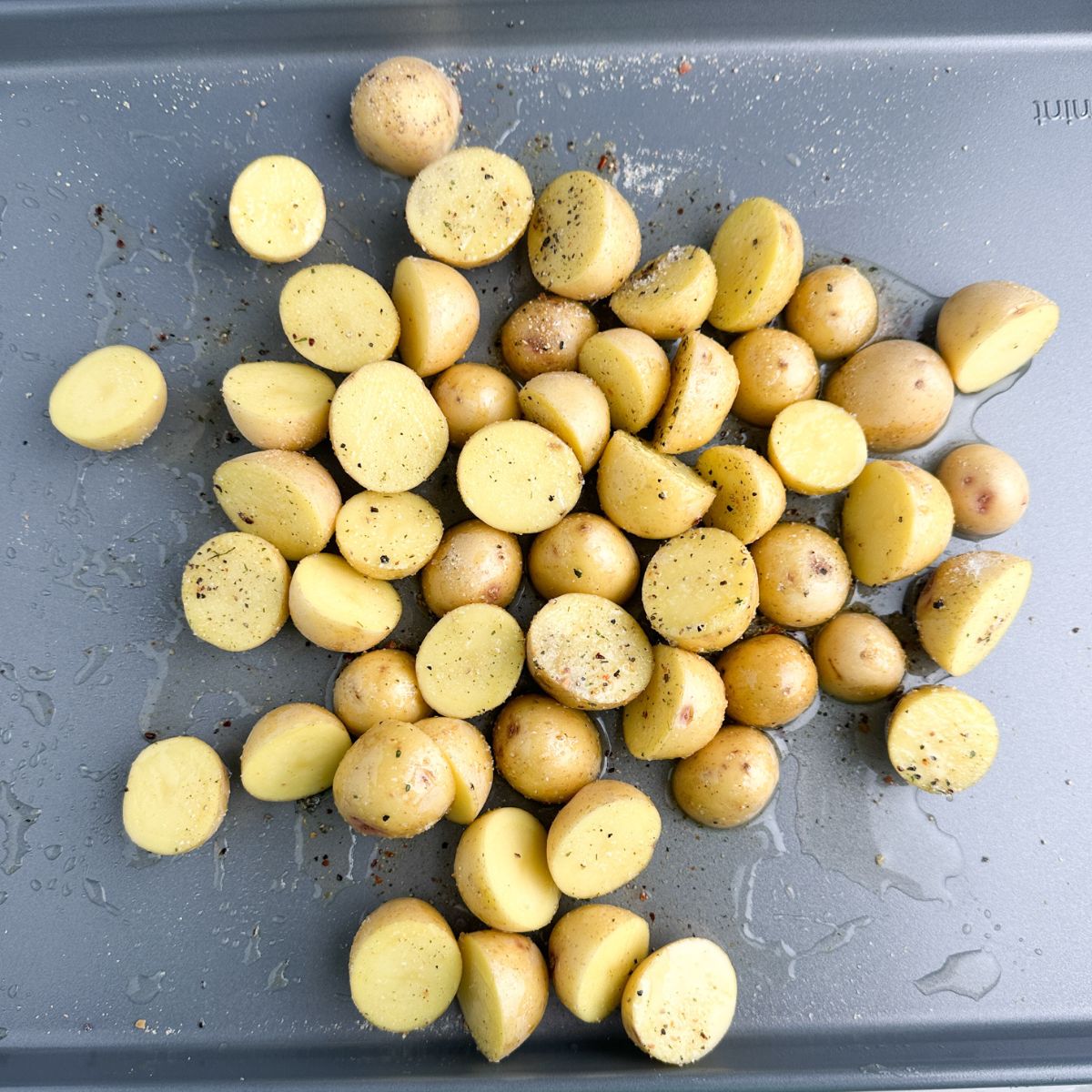 Mini potatoes cut in half on a baking sheet with oil. 