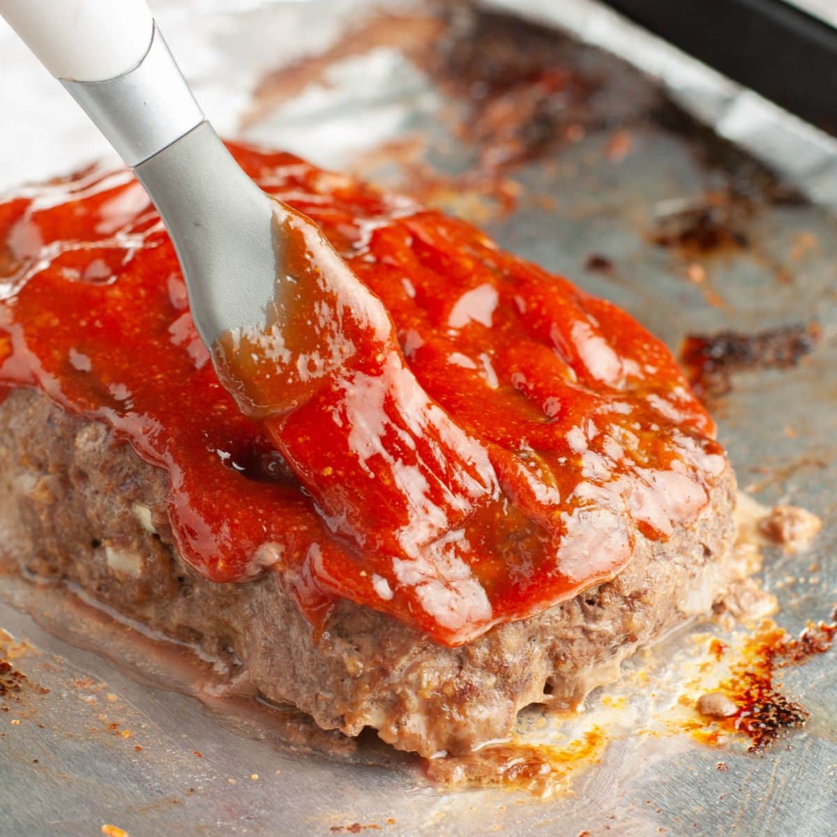 Brushing meatloaf glaze on a meatloaf.