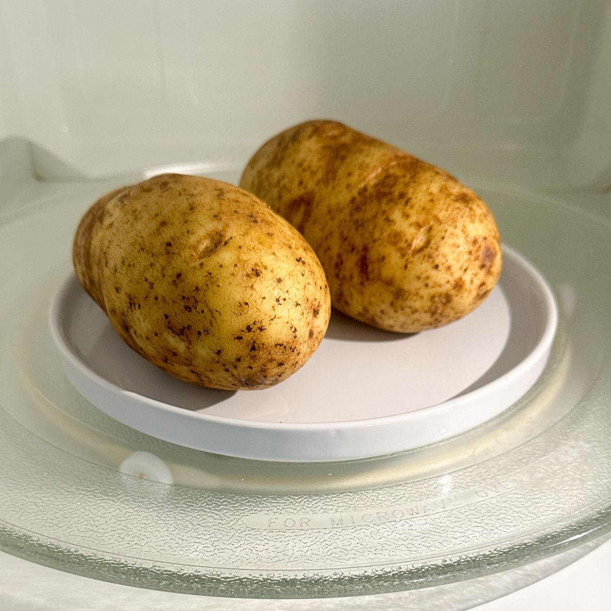 Two potatoes on a plate in the microwave.