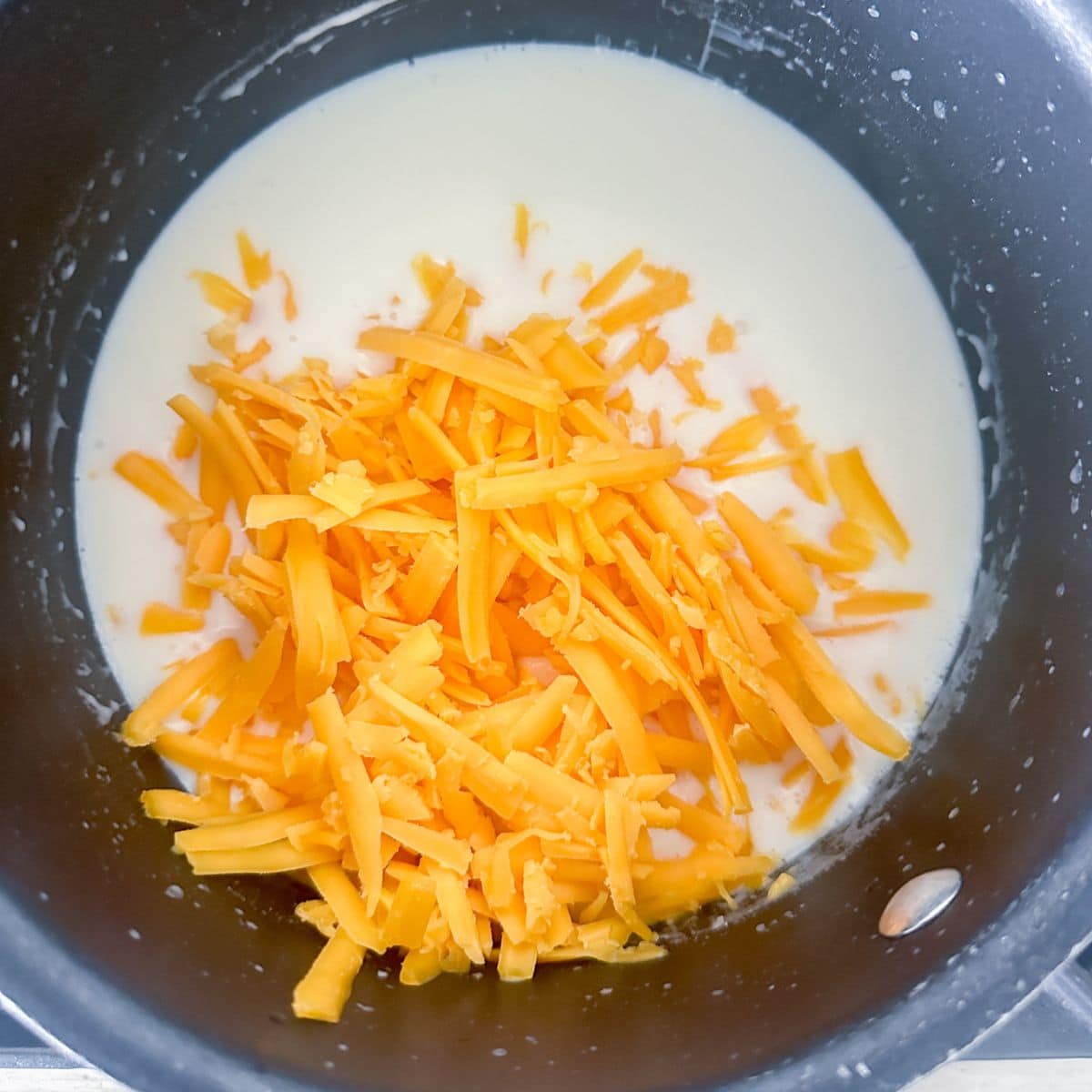 Pot with shredded cheese and milk.