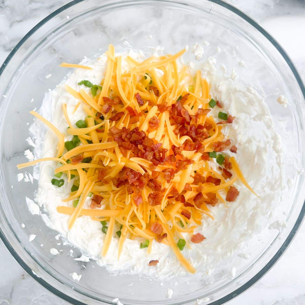 Bowl with cream cheese, shredded cheese, bacon bits, and green onion.