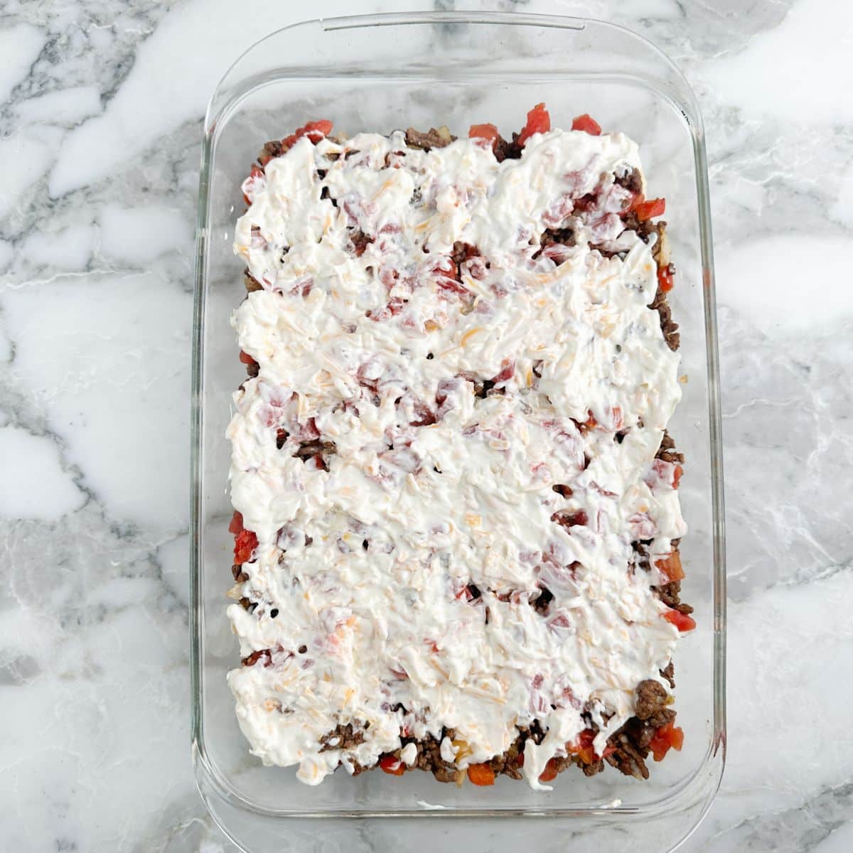 Ground beef casserole topped with sour cream in casserole dish.