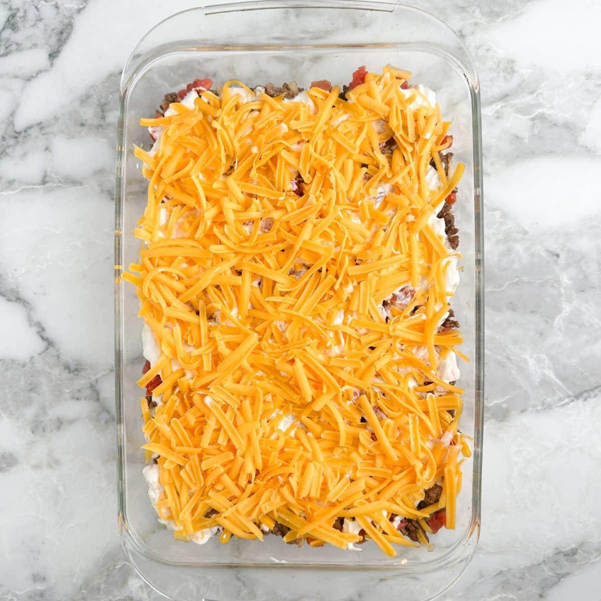 Casserole dish with ground beef casserole and shredded cheese.