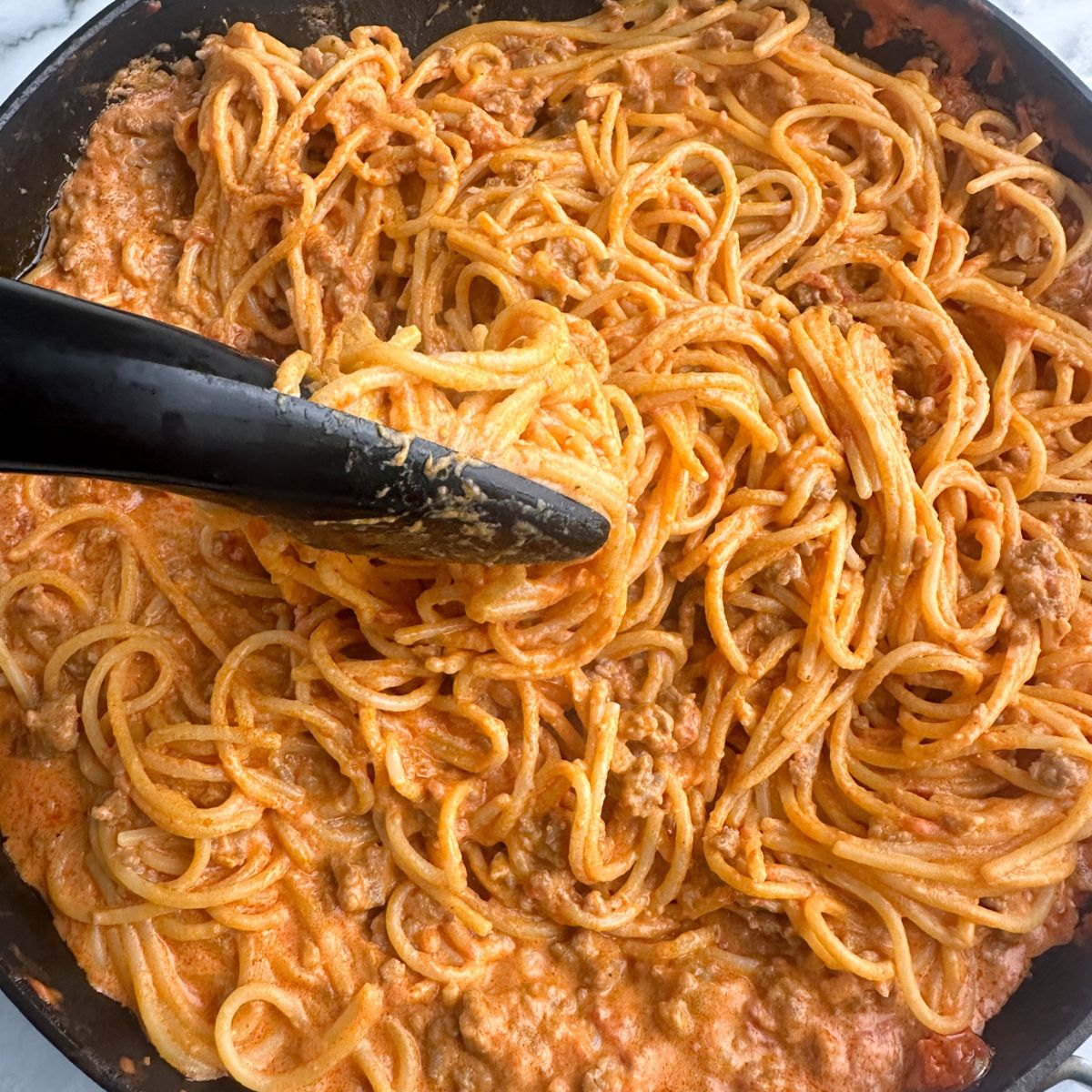 Skillet with creamy spaghetti in tongs. 