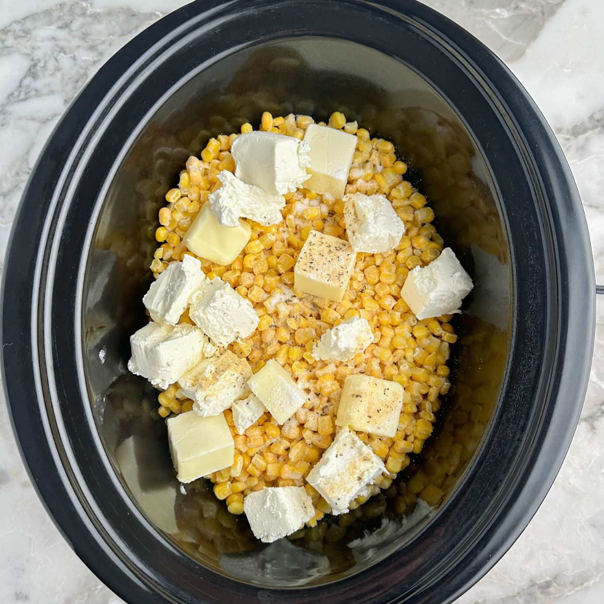 Slow cooker with corn, cream cheese, and butter.