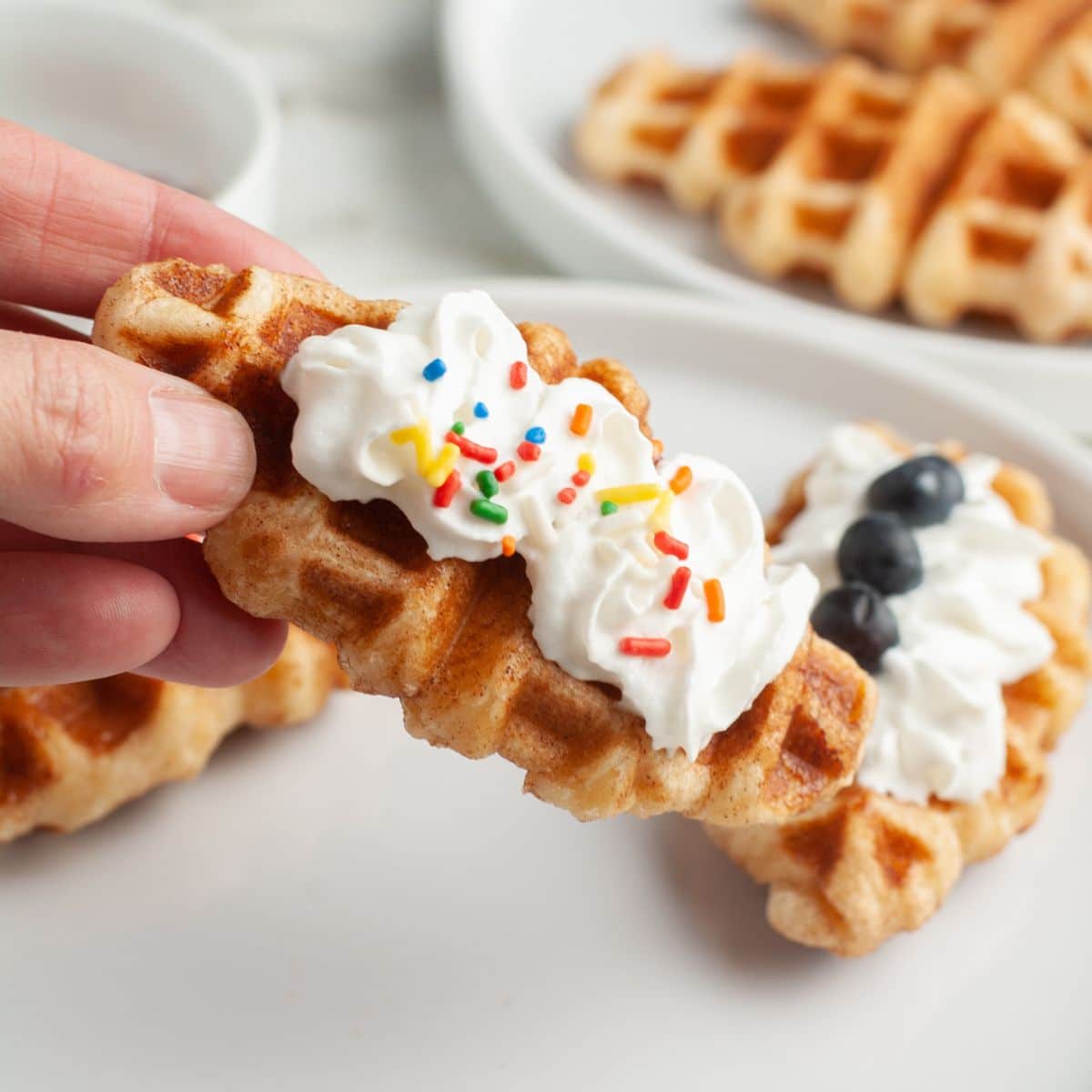 Hand holding a croffle topped with whipped cream and sprinkles.