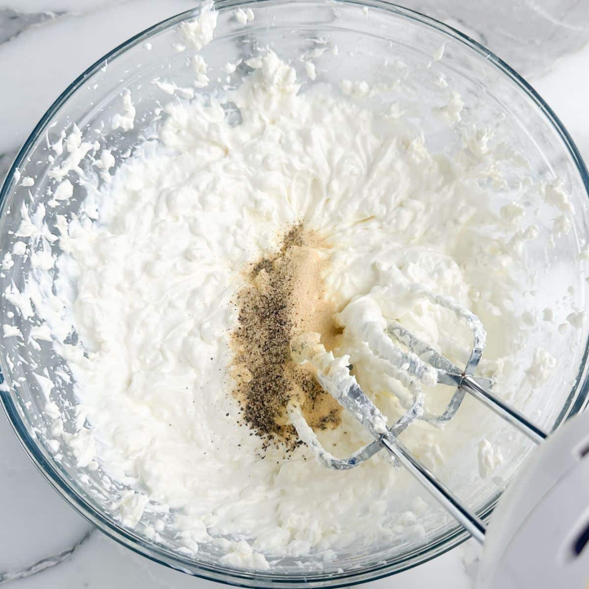 Bowl of beaten cream cheese with seasonings and mixer.