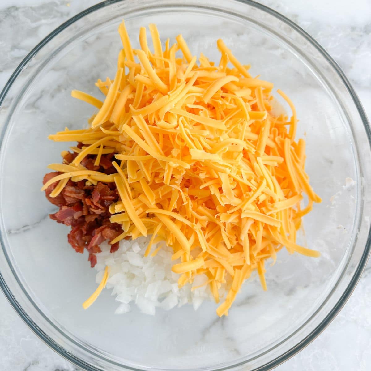 Bowl with diced onion, bacon bits, and shredded cheese. 