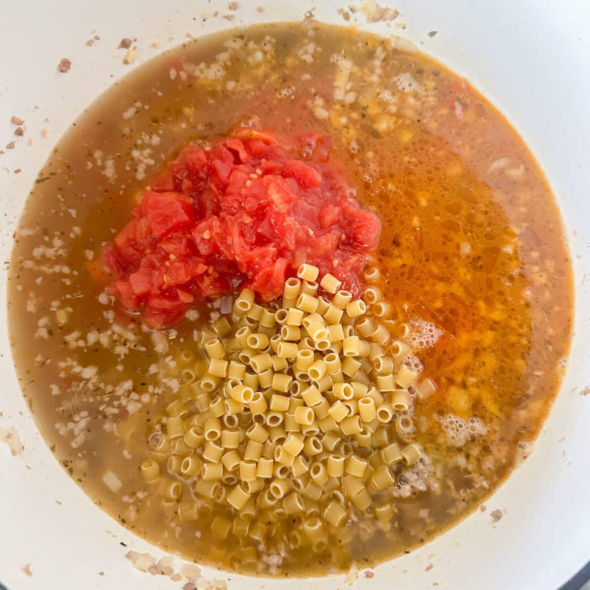 Pot with broth, diced tomatoes, and pasta.