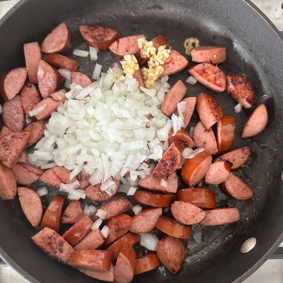 Cut kielbasa sausage with diced onion in a skillet.