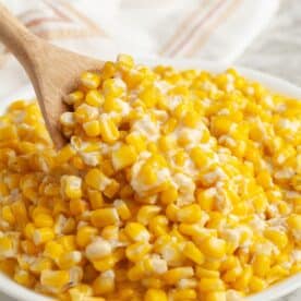 Bowl of creamy corn with a wooden spoon.