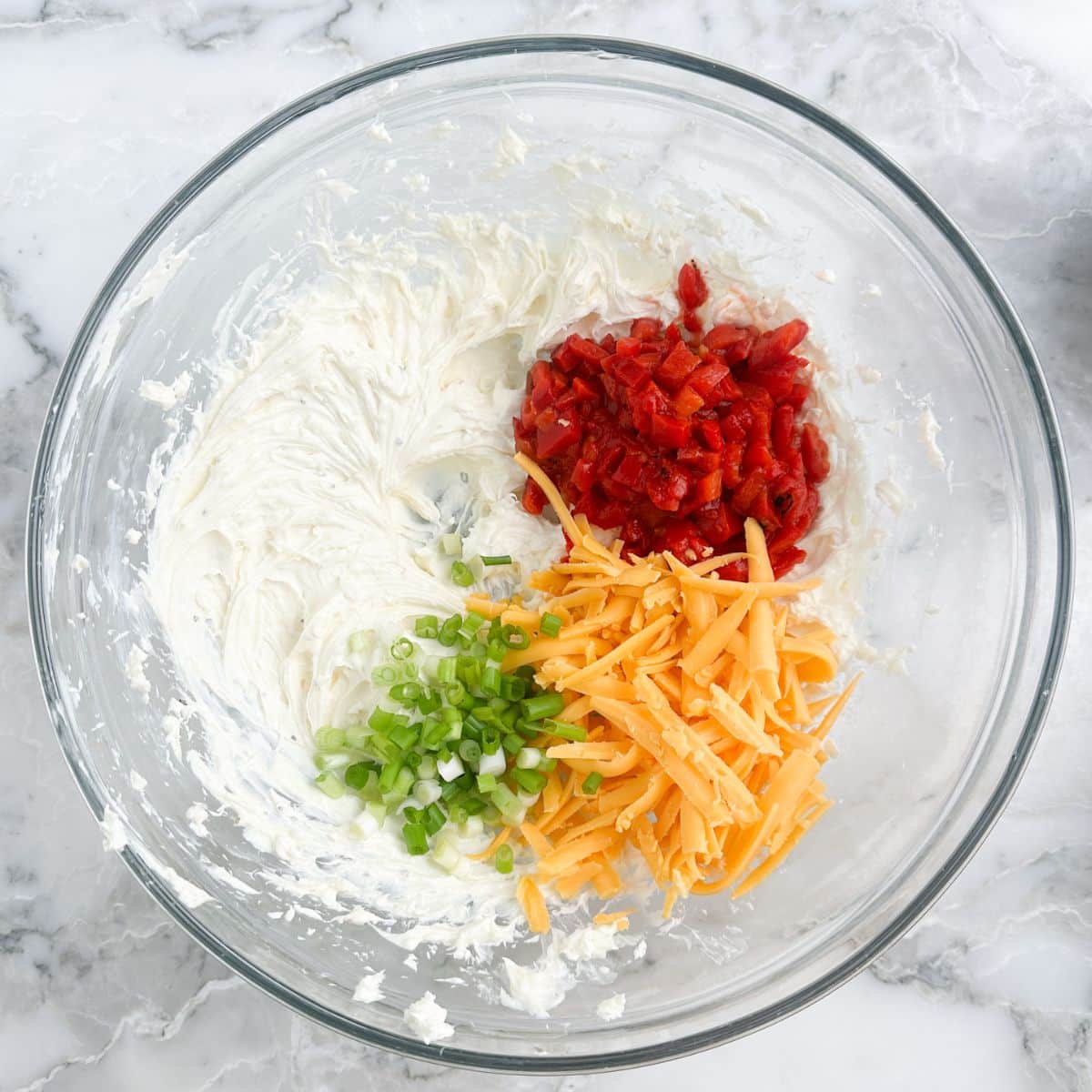 Bowl of whipped cream cheese, roasted red pepper, diced green onion, and shredded cheese.