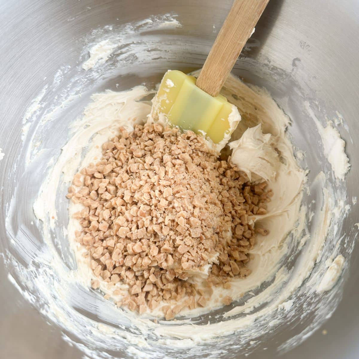 Bowl with cream cheese and toffee bits with a spatula.