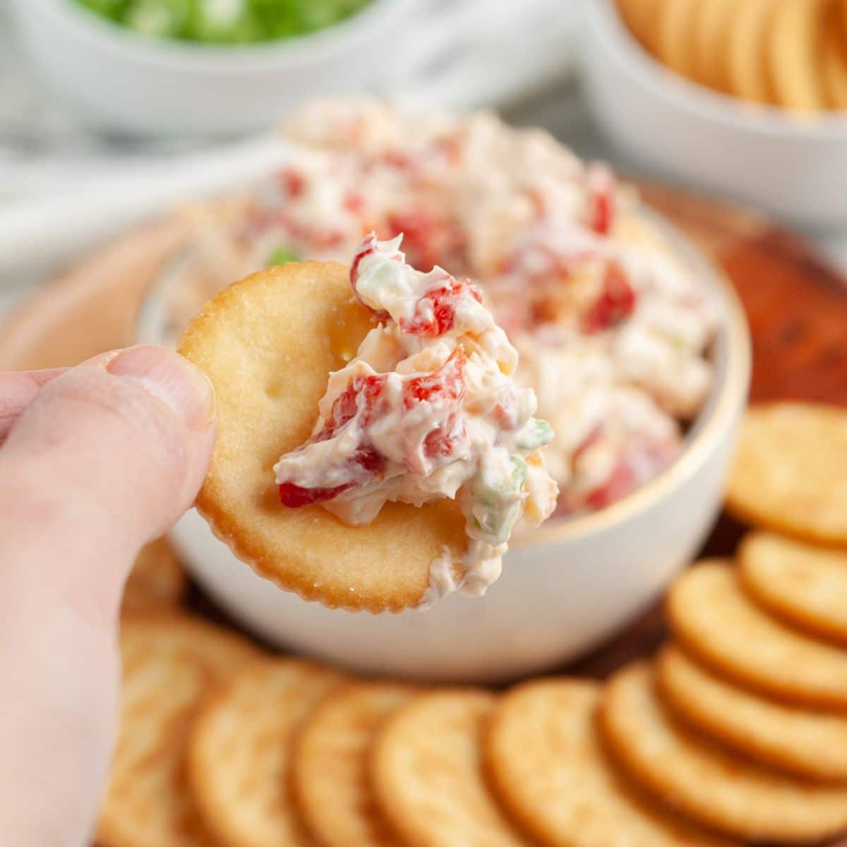 Bowl of creamy roasted red pepper dip with a hand holding a cracker with the dip. 