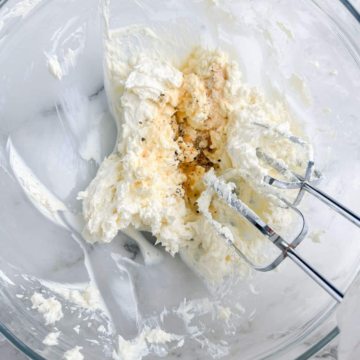 Bowl of whipped cream cheese with seasoning and a mixer. 